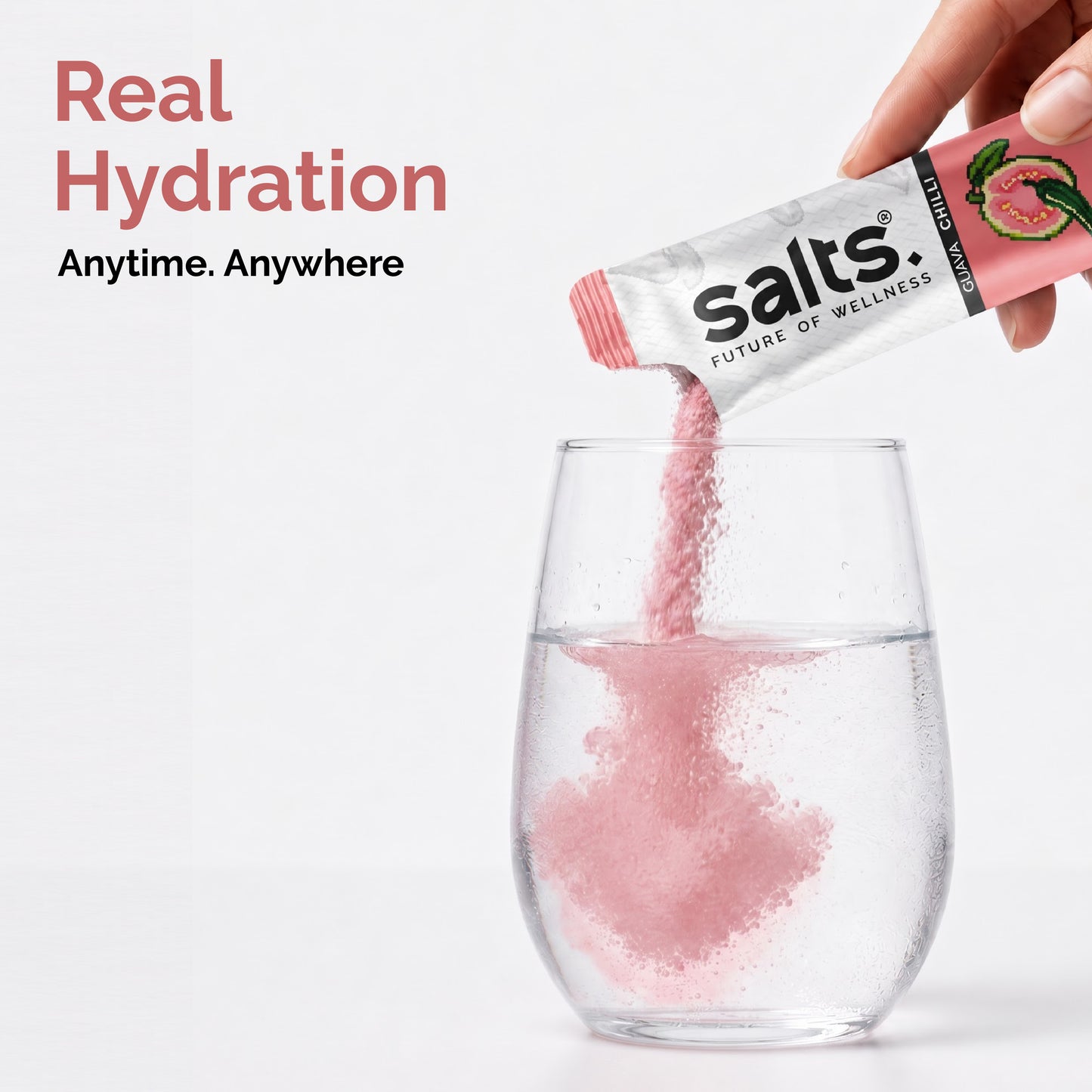 A hand pours pink salt from a packet labeled 'Guava Chilli Salts' into a clear glass of water, with the text 'Real Hydration Anytime. Anywhere' on the left.